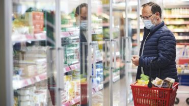 Photograph of a man in a mask shopping at a grocery store.