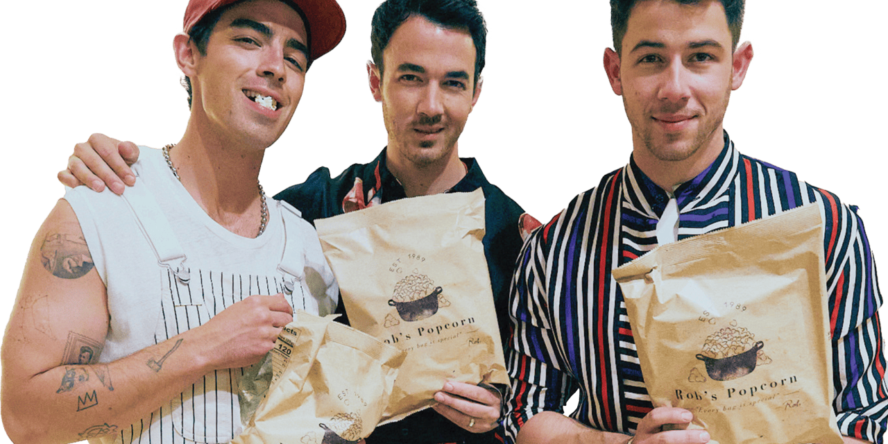 Photograph of the Jonas Brothers holding bags of Rob's Backstage Popcorn.