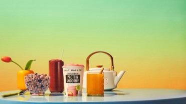 Daily Harvest smoothie, elixir and oat bowl on a blue table against a green and yellow background.